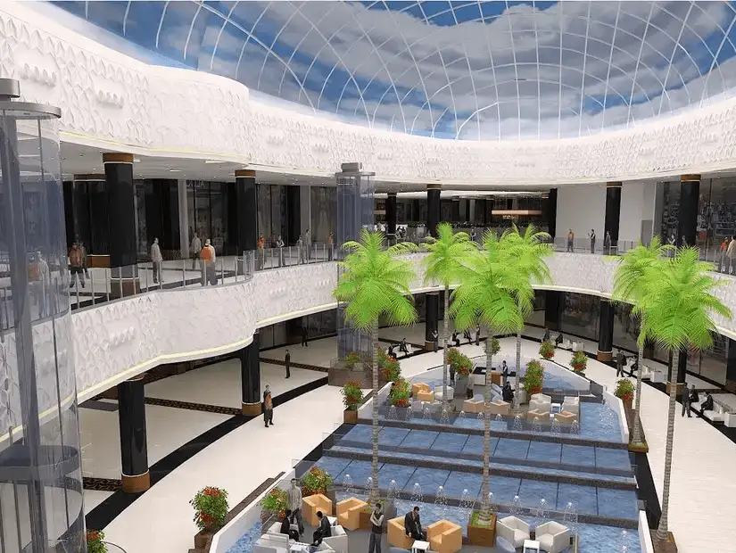 The spacious interior of a shopping mall with palm trees and a skylight.