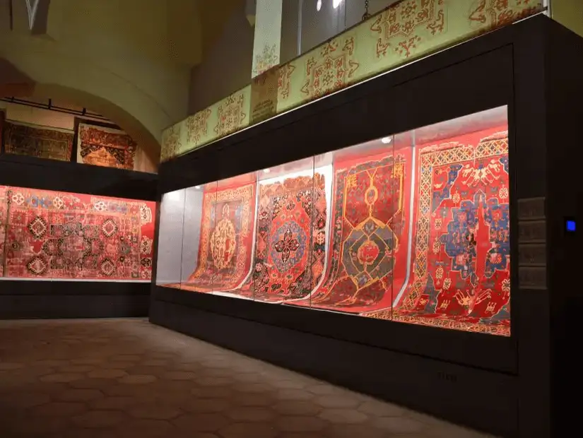 A display of traditional carpets inside a museum, showcasing intricate patterns and vibrant colors.