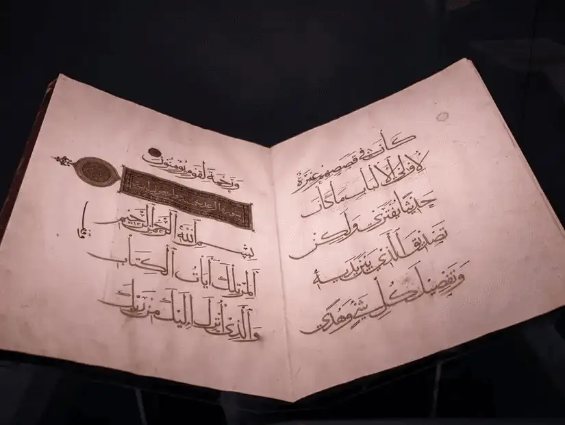 An ancient manuscript displayed in a glass case, showcasing beautiful Arabic calligraphy.
