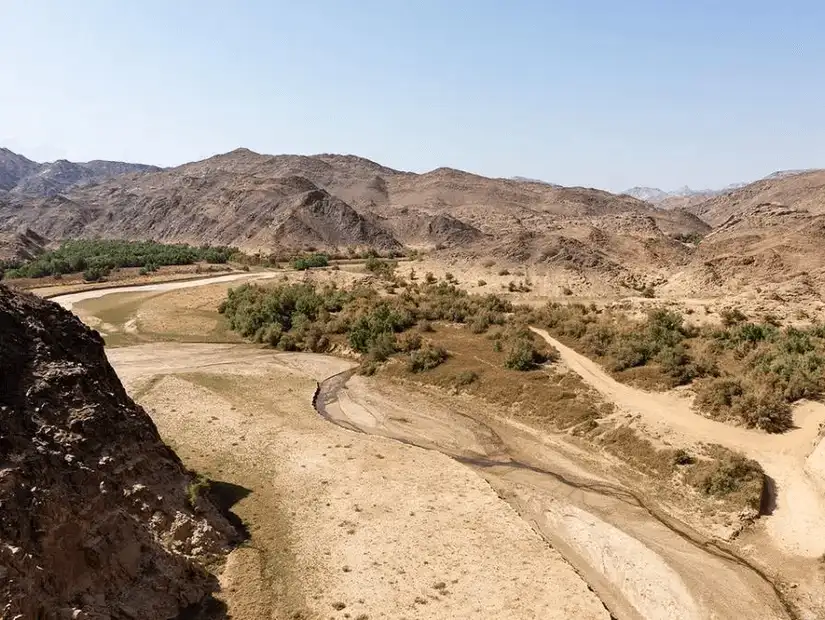 A vast desert valley with traces of water winding through Najran's rocky landscape.