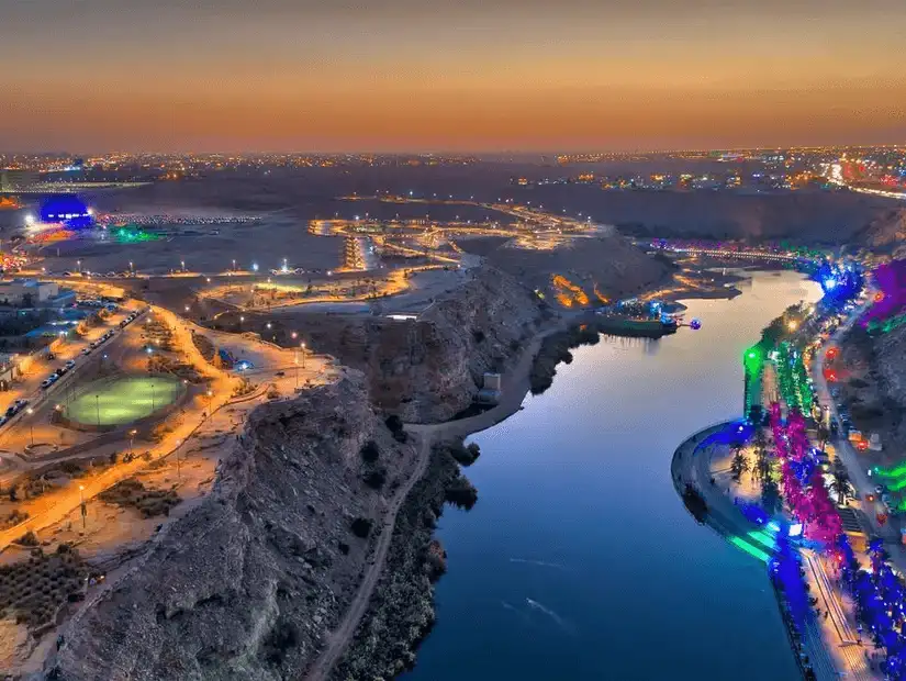 Wadi Namar at sunset, showcasing vibrant city lights and the tranquil water.