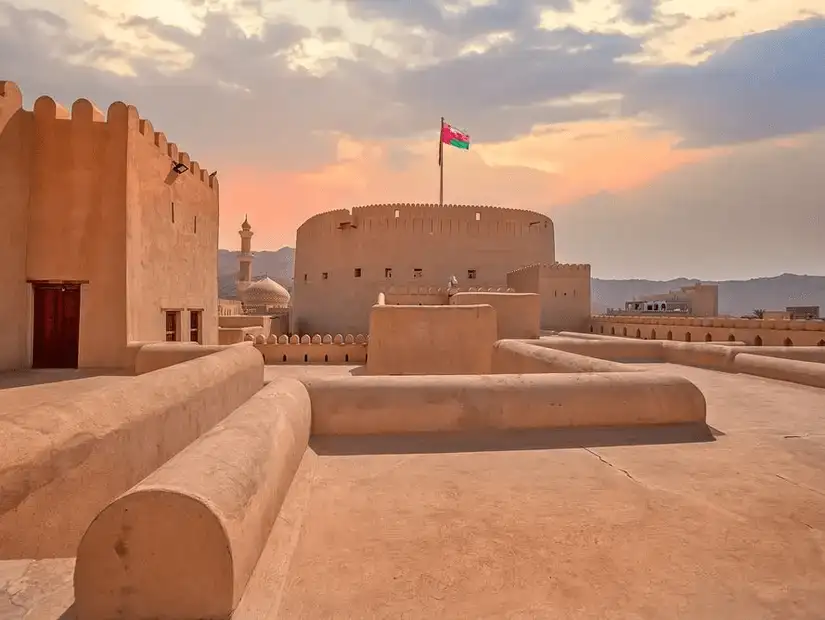 The historic Nizwa Fort standing tall under the Omani flag, offering a glimpse into Oman’s rich past.