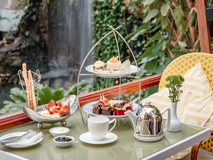 Afternoon tea with an array of desserts and tea at Noor Lounge, set against lush greenery.