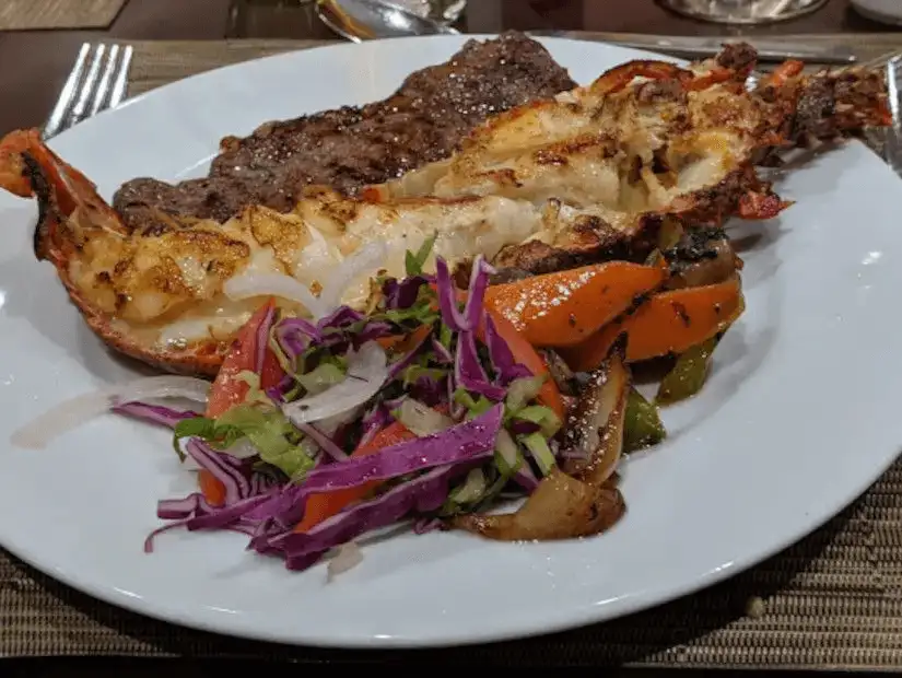 A delicious surf and turf combo featuring grilled lobster tail and steak, accompanied by sautéed vegetables and a fresh salad.