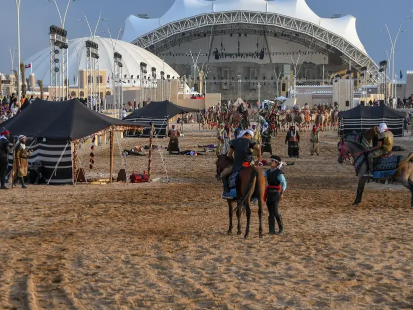 A lively outdoor festival with tents, horses, and a modern stage in the background.