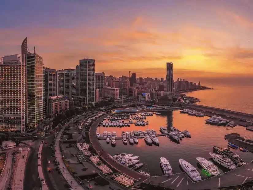 A stunning sunset view of Beirut's Olive Bay, reflecting on the water, surrounded by luxury yachts and the city skyline.