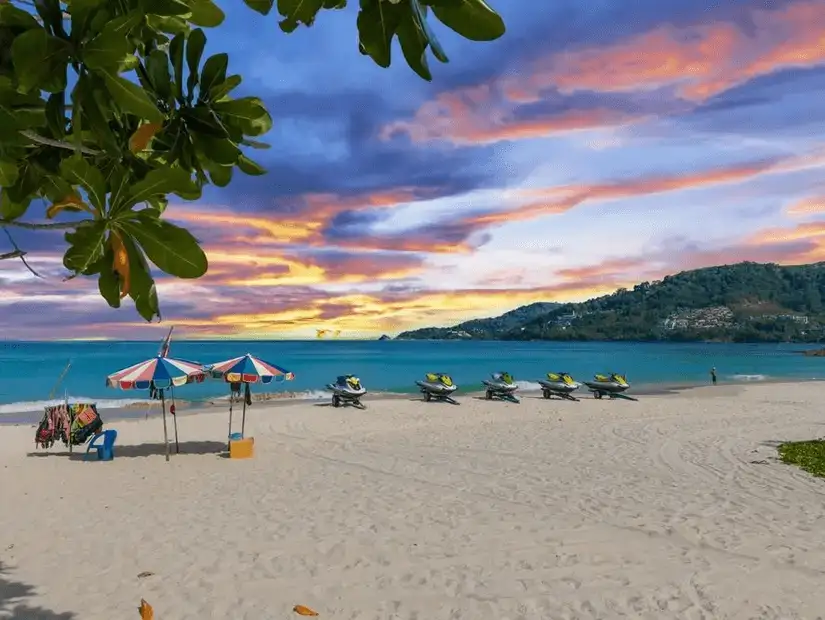 Patong Beach at sunset, with jet skis lined up on the sandy shore.