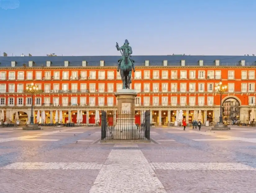 A historic square lined with red façades, cafes, and the statue of King Philip III.