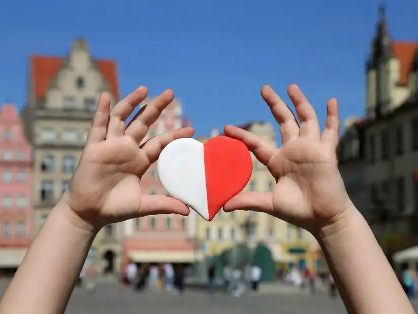 Heart-shaped cookie held up against the backdrop of colorful buildings in a Polish city square, symbolizing love for the culture.