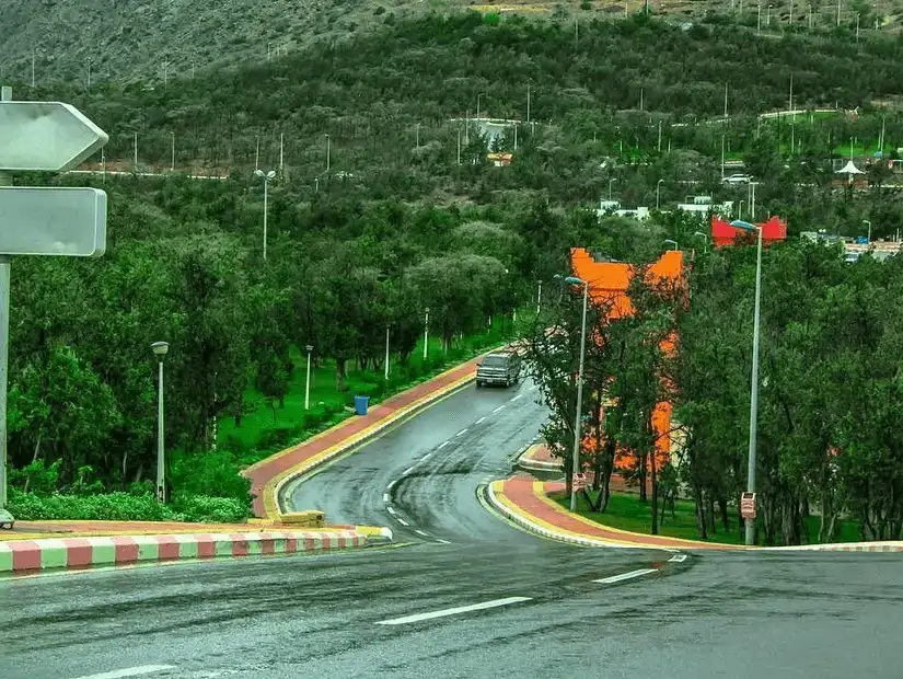 A quiet road surrounded by lush trees in Raghadan Forest.