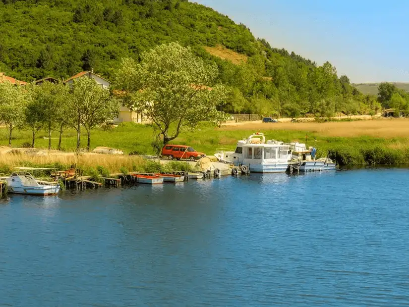 A peaceful riverside view in Riva, with clear blue water, small boats, and green landscapes.