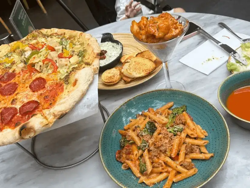 Pizza, pasta, and appetizers served on a marble table.