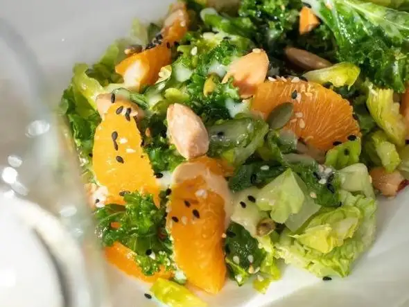 A vibrant and refreshing mix of citrus and green salad, sprinkled with sesame seeds.