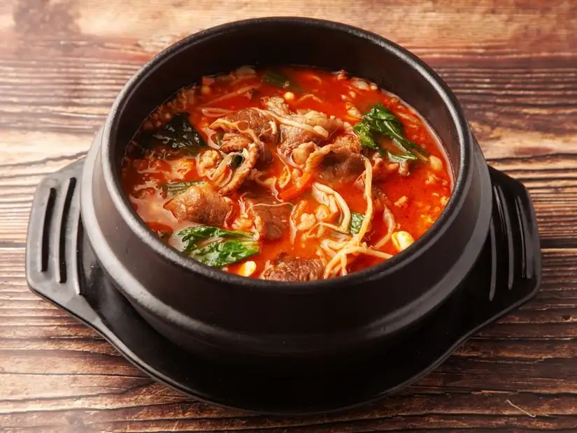 Spicy Korean stew with tender beef slices and fresh vegetables in a traditional black pot.