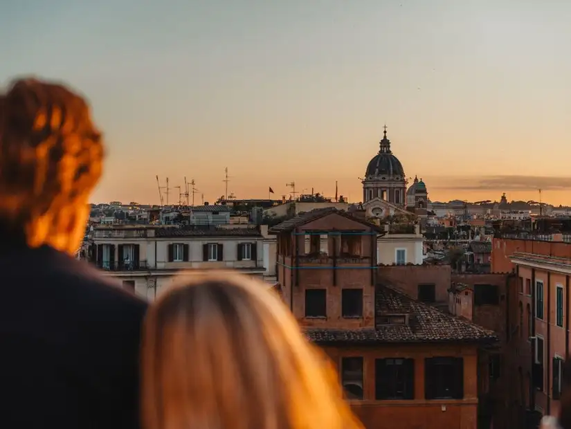 A couple admiring the sunset over the rooftops of Rome, with a church dome in the distance.