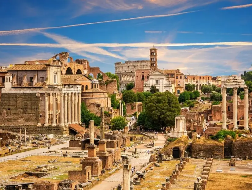 The ancient Roman Forum with ruins of temples, columns, and historical structures against a bright sky.