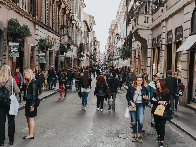A busy street in Rome with people walking between fashionable shops and historic buildings.