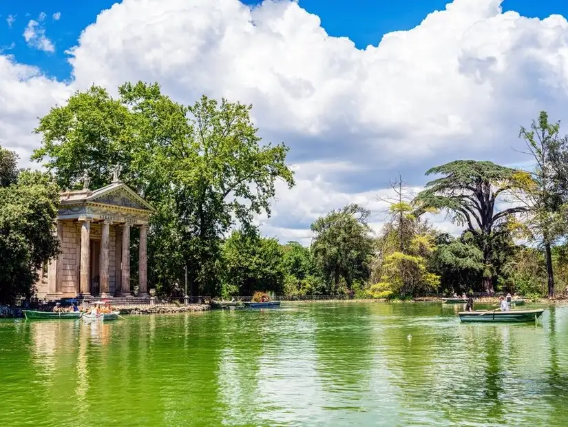 A peaceful green pond with boats and a classical monument in a serene landscape.