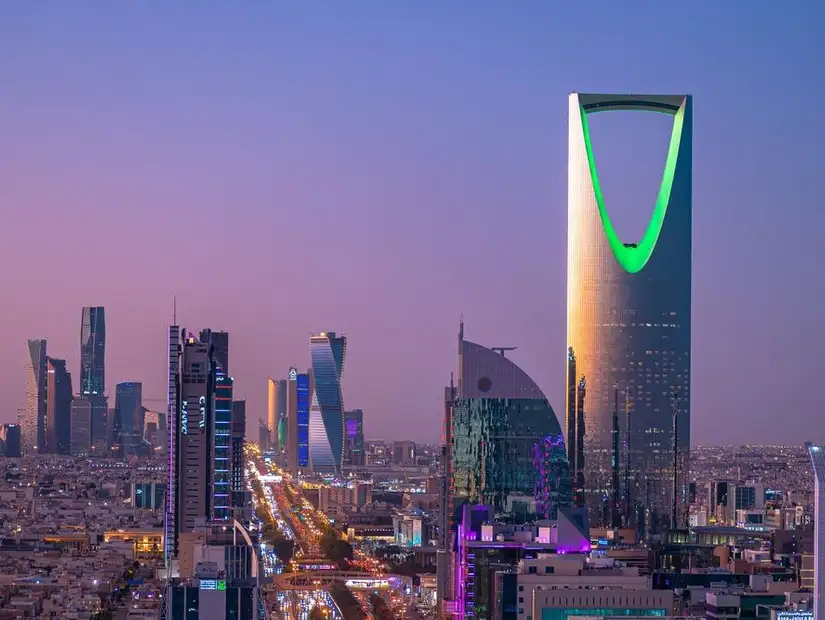 Riyadh skyline at twilight, highlighted by the glowing green of the Kingdom Centre tower amidst the urban expanse.