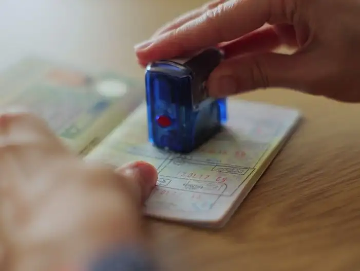 Opened passport displaying visa stamps, held in hand at an airport.