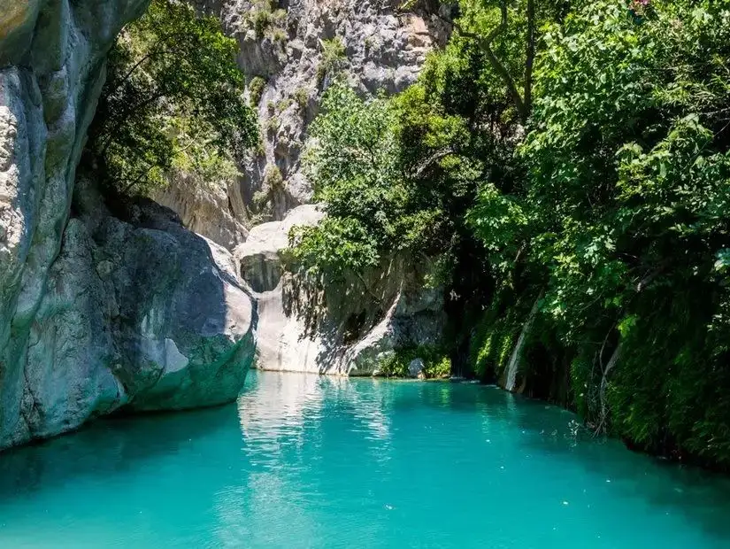 A serene image from Saklikent National Park showcasing the lush green landscape, blue waters, and towering cliffs, offering a tranquil escape into nature.