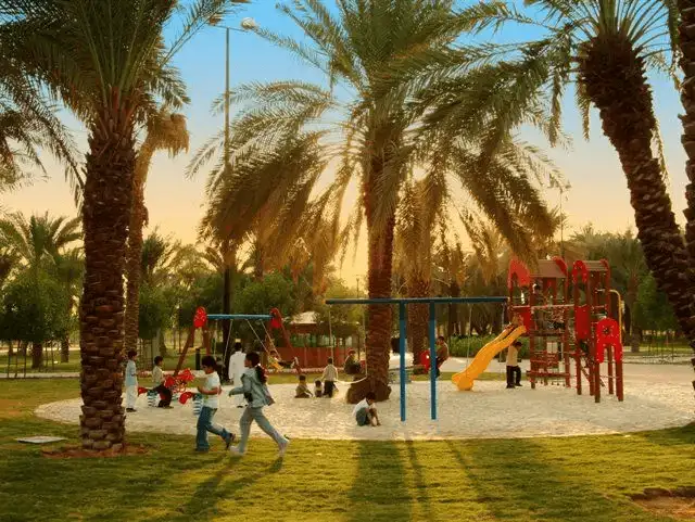 Children enjoying playtime at a park with swings and slides surrounded by palm trees.