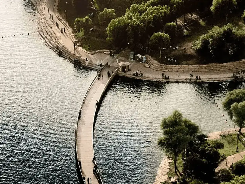 A curved walkway over a serene lake, with people strolling along the water's edge.