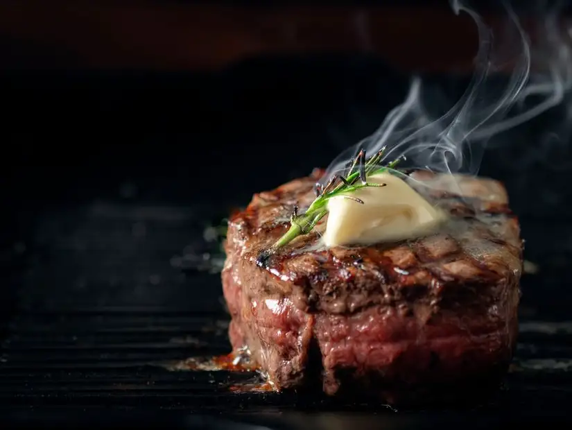 Sizzling steak topped with a melting pat of butter and fresh herbs, creating an inviting aroma.