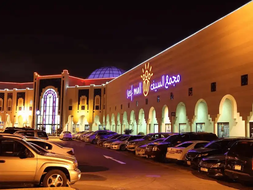 Seef Mall glowing in the night, with a large parking lot and warmly lit exterior.