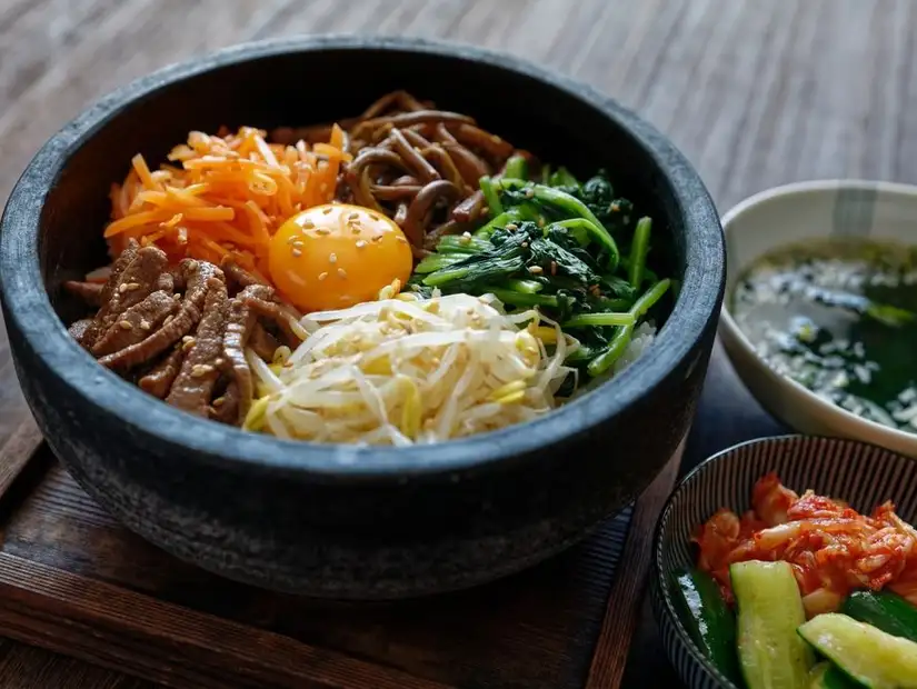 Traditional Korean bibimbap with assorted vegetables, beef, and a sunny-side-up egg in a hot stone bowl.