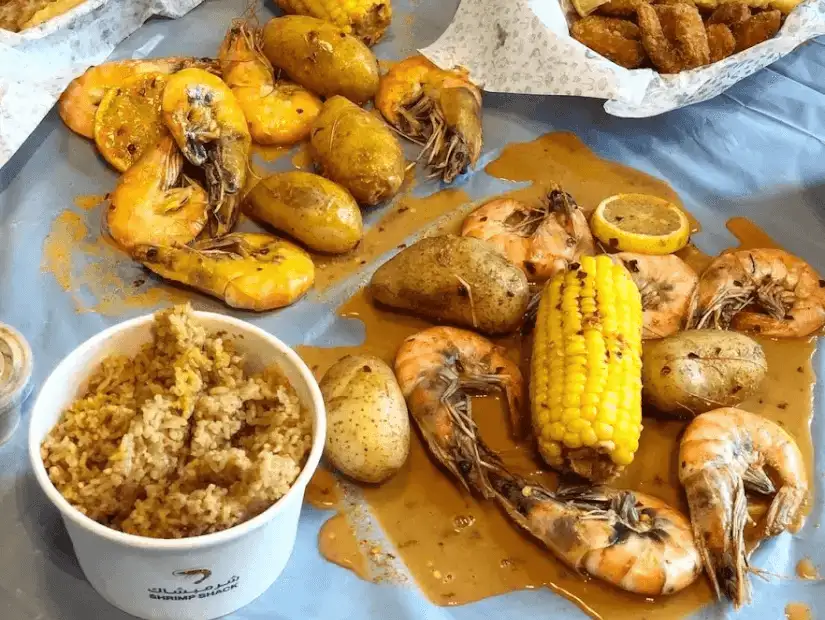 A hearty seafood platter from Shrimp Shack, featuring succulent shrimp, corn on the cob, and potatoes drenched in rich, flavorful sauce.