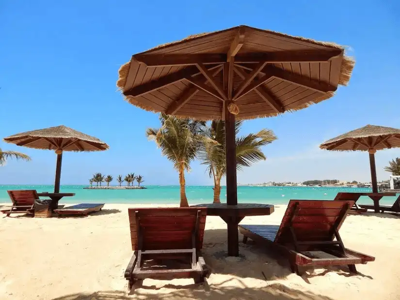 Comfortable wooden sun loungers shaded by traditional umbrellas, offering a relaxing beachside view.