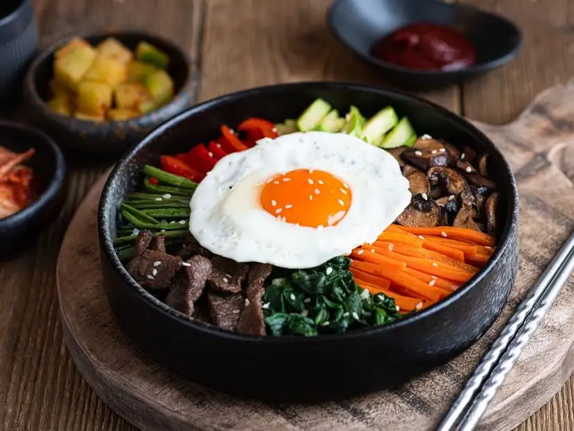 Classic bibimbap with vibrant vegetables, beef, and a fried egg, served in a hot stone bowl with side dishes.