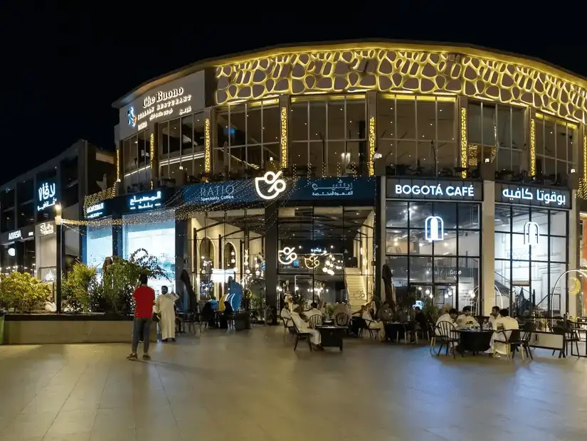 A bustling outdoor shopping plaza with cafes and brightly lit restaurants.