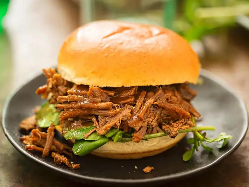 Tender pulled meat with greens on a soft round bun.