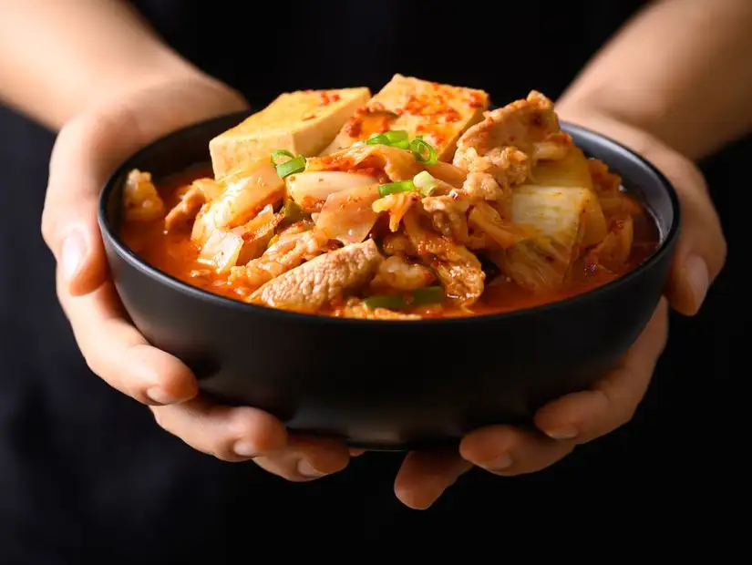 Spicy and hearty Korean tofu stew with vegetables and pork, held in a black ceramic bowl.