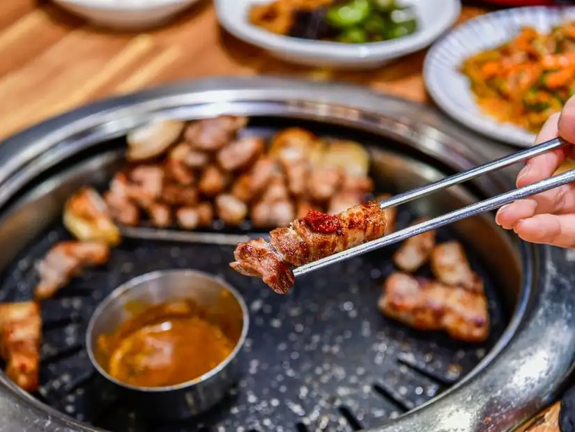 Juicy grilled pork belly pieces served with dipping sauce and side dishes at a Korean barbecue.