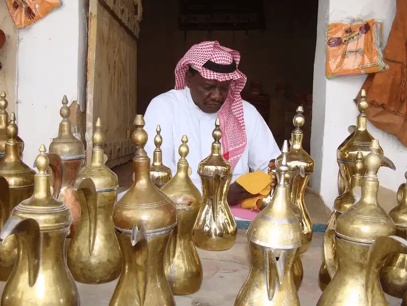 A vendor carefully polishing traditional brass coffee pots at a local market in Najran, highlighting the region's craftsmanship.