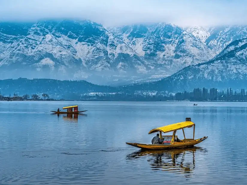 A picturesque view of Srinagar with a boat on the calm Dal Lake and the surrounding mountains in the background.