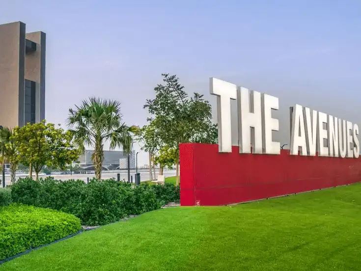 A modern shopping destination with large 'The Avenues' signage, surrounded by greenery and palm trees.