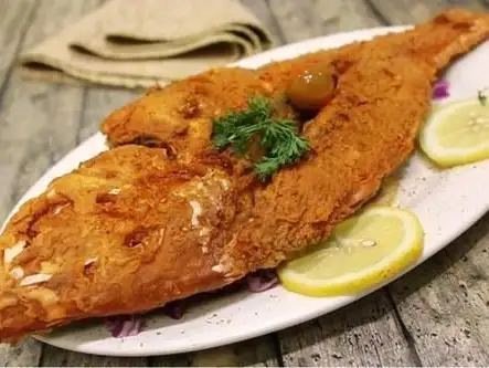 A rustic presentation of a whole fish, fried to golden perfection and garnished with lemon slices and fresh herbs.