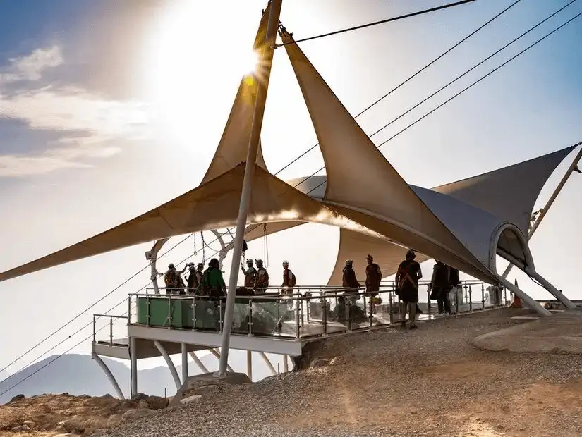 Helmeted adventurers gather on a sail-shaded platform atop Jebel Jais, poised to launch down the world-record zipline.