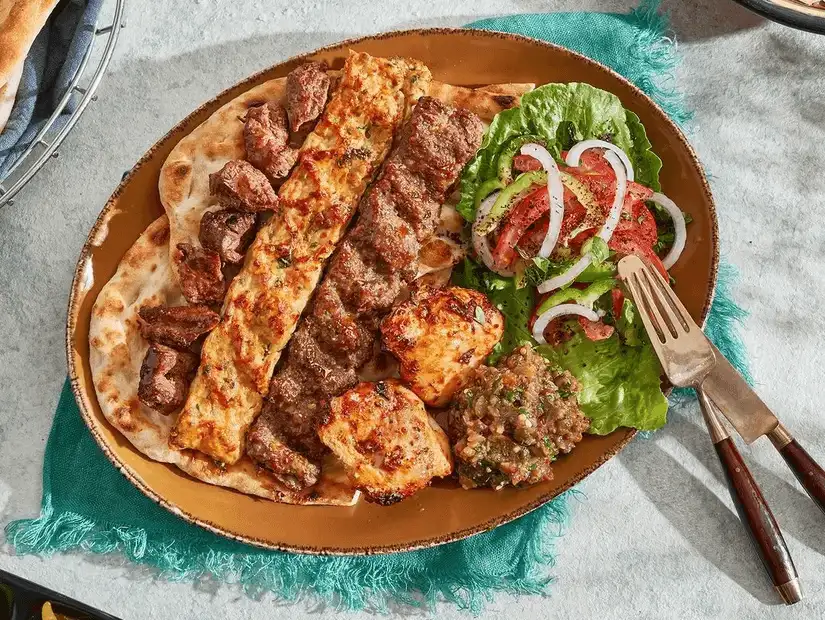 A hearty mixed grill platter with kebabs, chicken, and beef served alongside fresh salad and dips.