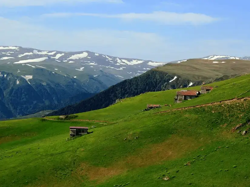 Picturesque highland pastures with scattered huts and snow-capped mountains.