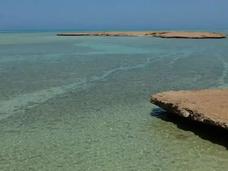 Crystal-clear waters gently lap against a rocky outcrop on the tranquil shores of Umm Sahar.