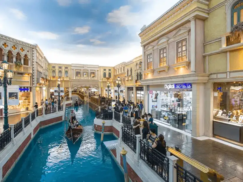 Gondolas glide through a shopping arcade under a painted sky.