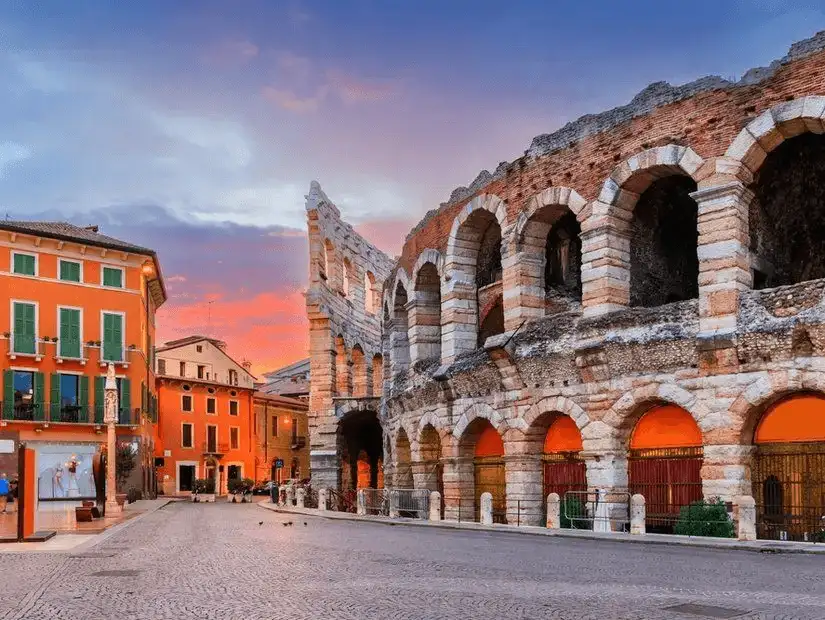 Twilight falls over the ancient Roman arena in Verona, casting a warm glow on the historic structure and surrounding streets.