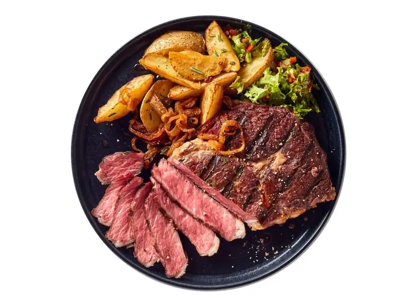 Perfectly cooked steak served with golden roasted potatoes and fresh salad on a dark ceramic plate.