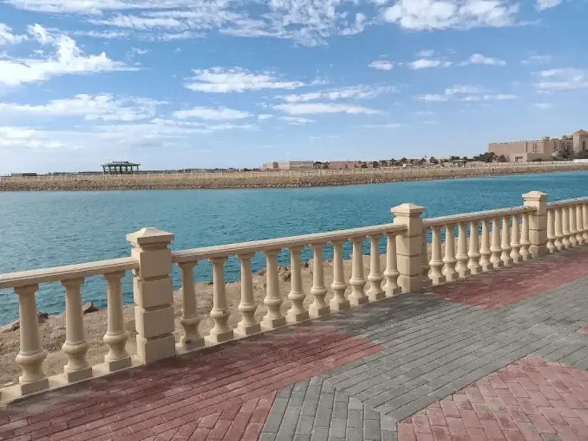 A picturesque waterfront with a stone railing and clear blue water under a partly cloudy sky.