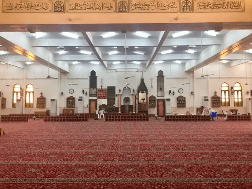 A spacious mosque interior with intricate decorations and red carpet.